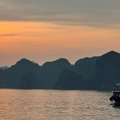 Impresionante atardecer sobre la bahía de Lan Ha, visto desde un crucero en Cat Ba, Vietnam, con el sol reflejándose en el agua y montañas kársticas al fondo.