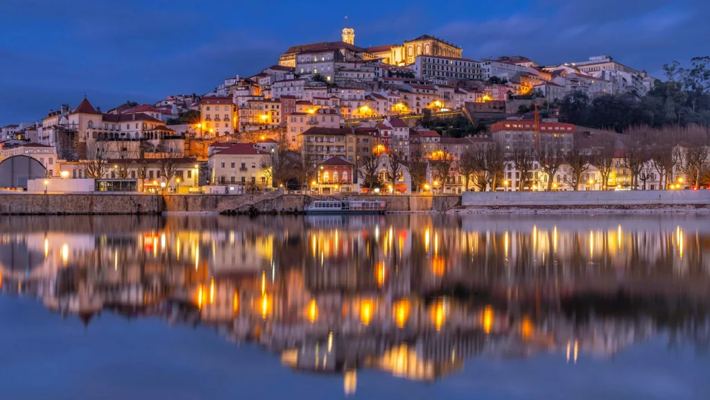 Coímbra iluminada de noche reflejándose en el río Mondego