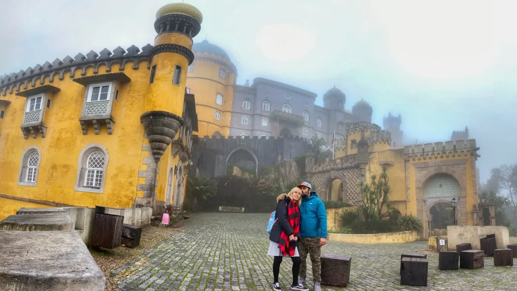 Pareja frente al Palacio da Pena en Sintra, rodeados de niebla y color