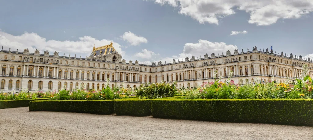 Fachada del Palacio de Versalles con jardines floridos bajo un cielo con nubes en París