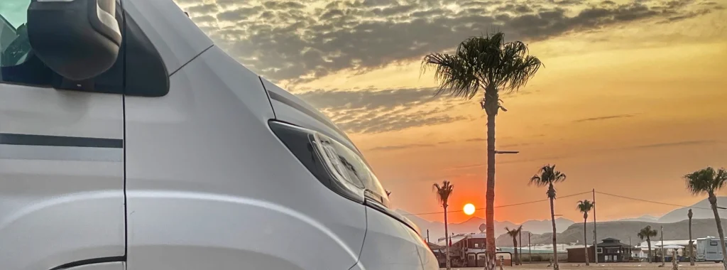 Atardecer con palmeras y camper en primera línea, puro viaje en autocaravana